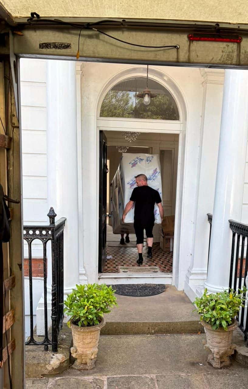 Two Duffield crew carrying a wrapped item through a columned porch