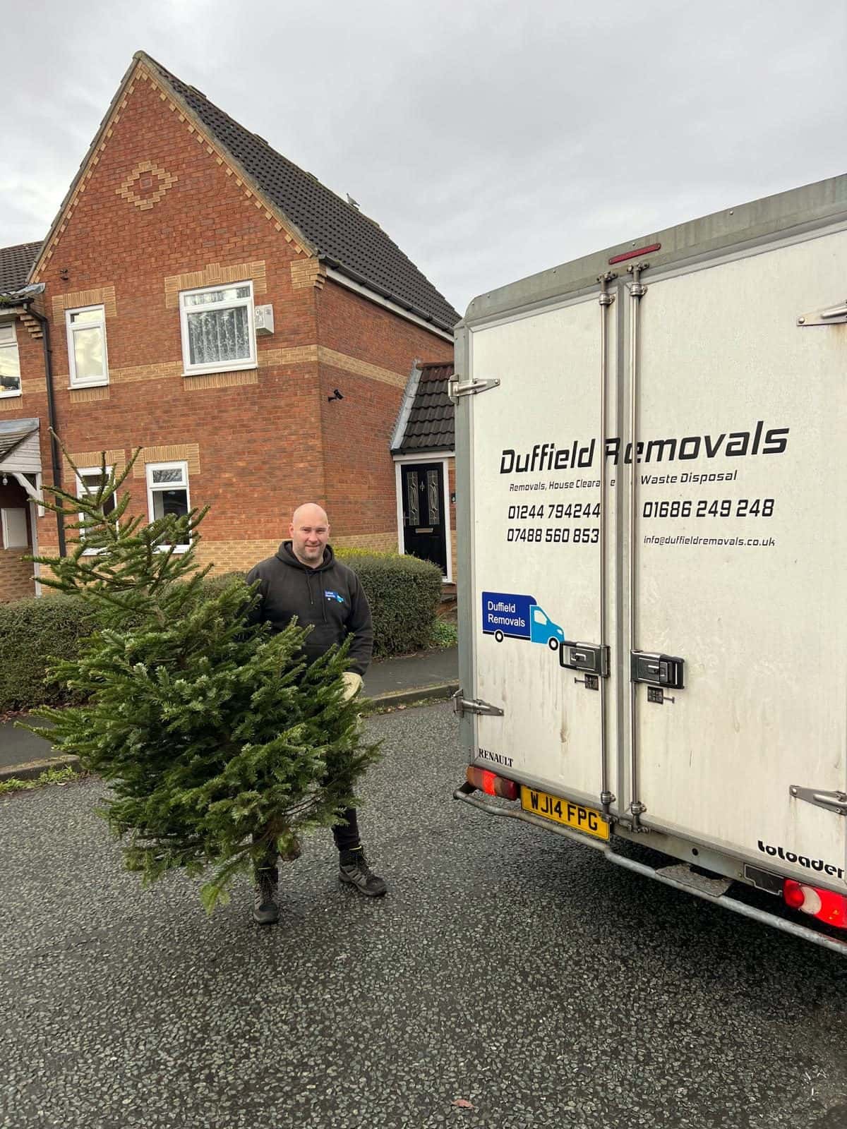 Duffield crew member holding a collected Christmas tree beside the van