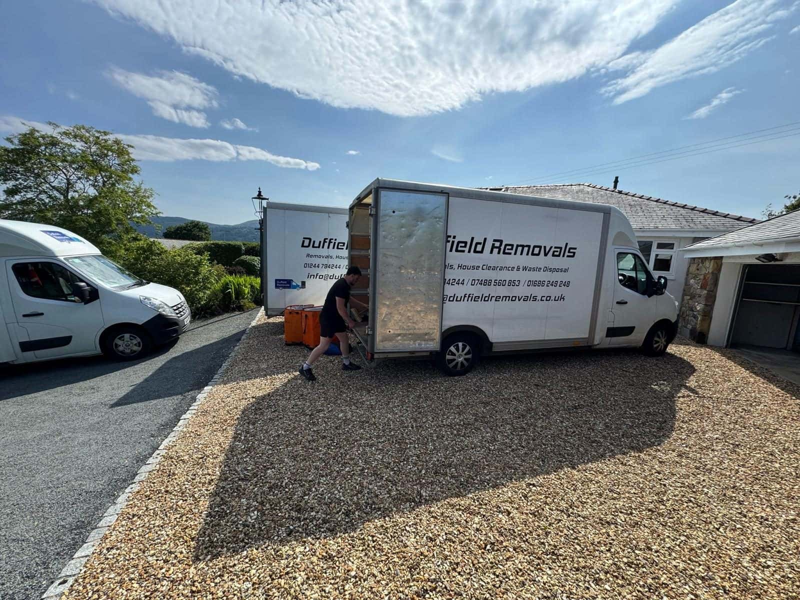 Duffield crew member pulling out a loading ramp, three vans on the drive