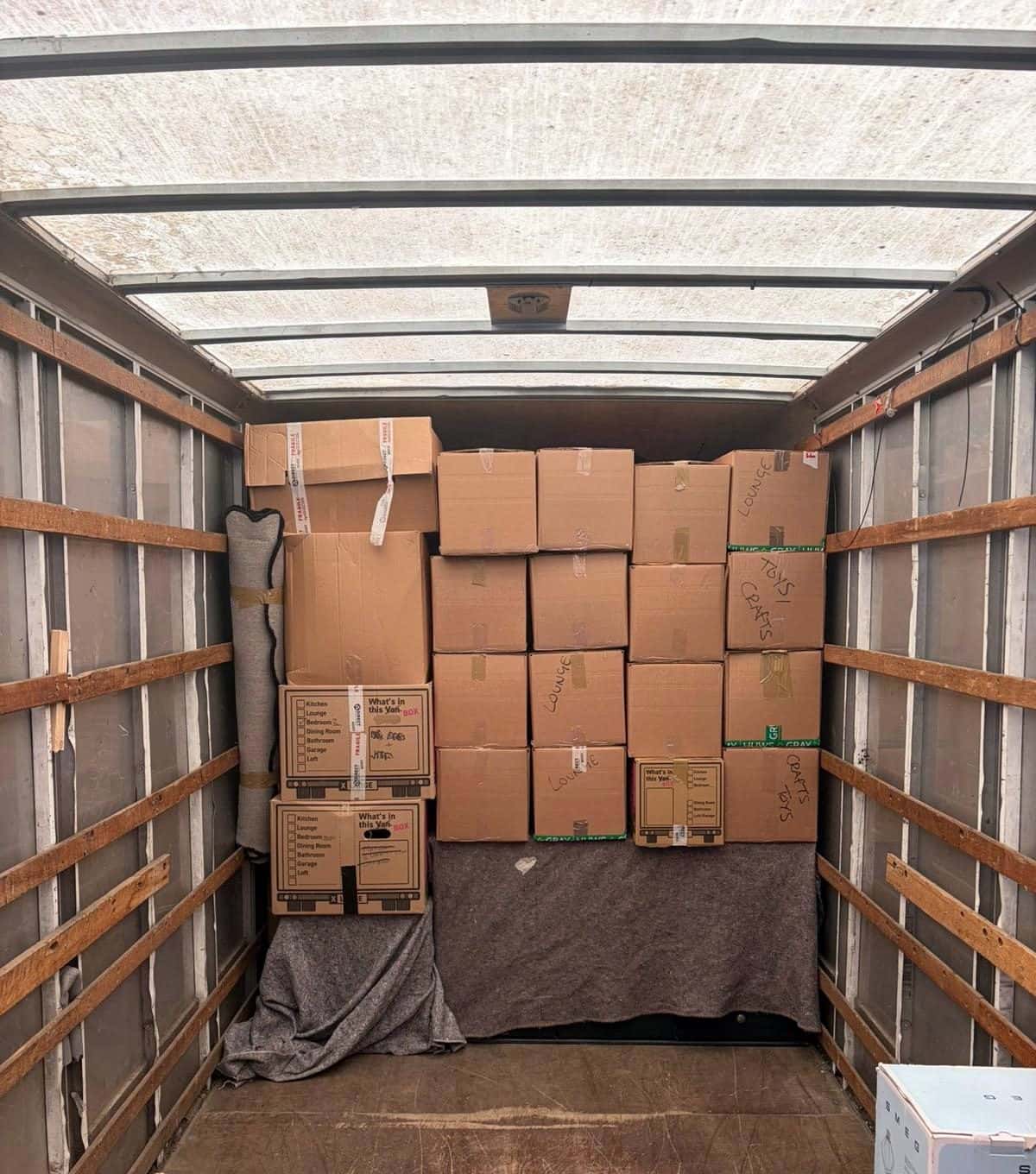 Boxes labelled lounge and toys stacked on blankets inside a removal van