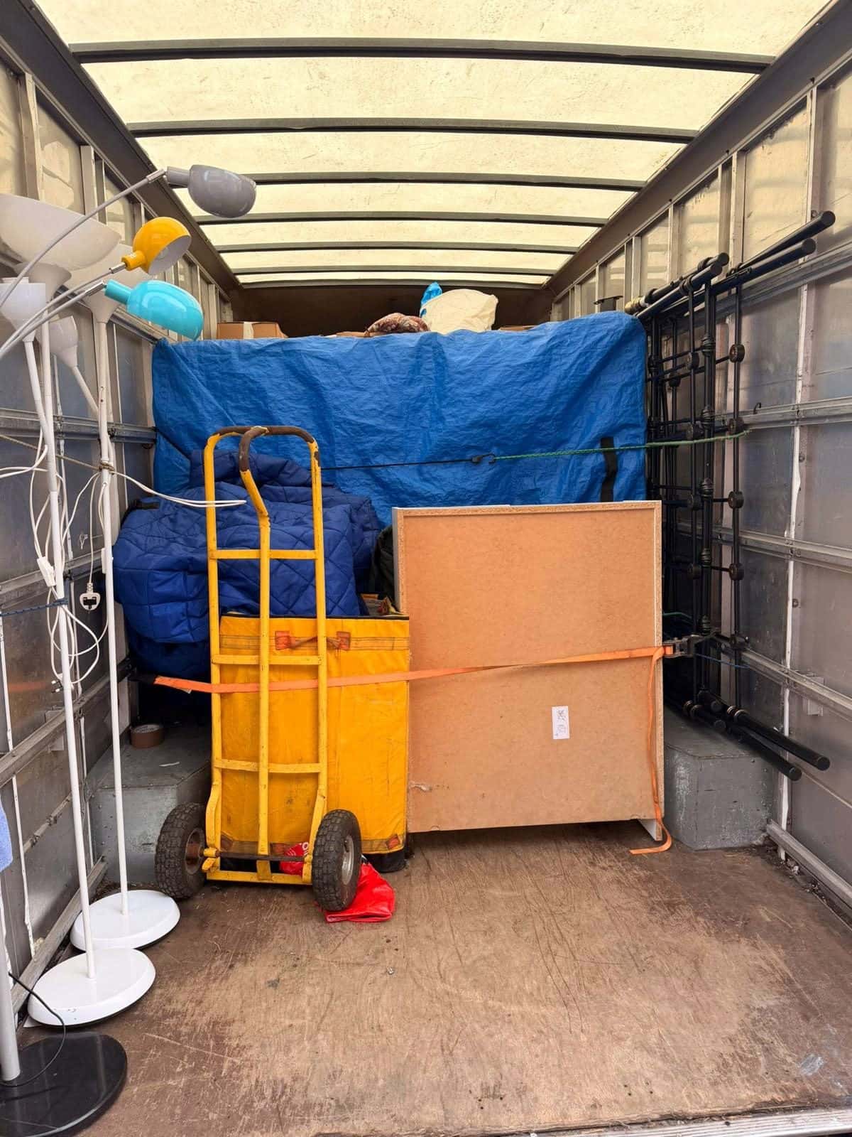 Load in a van secured with an orange ratchet strap, blankets and sack truck