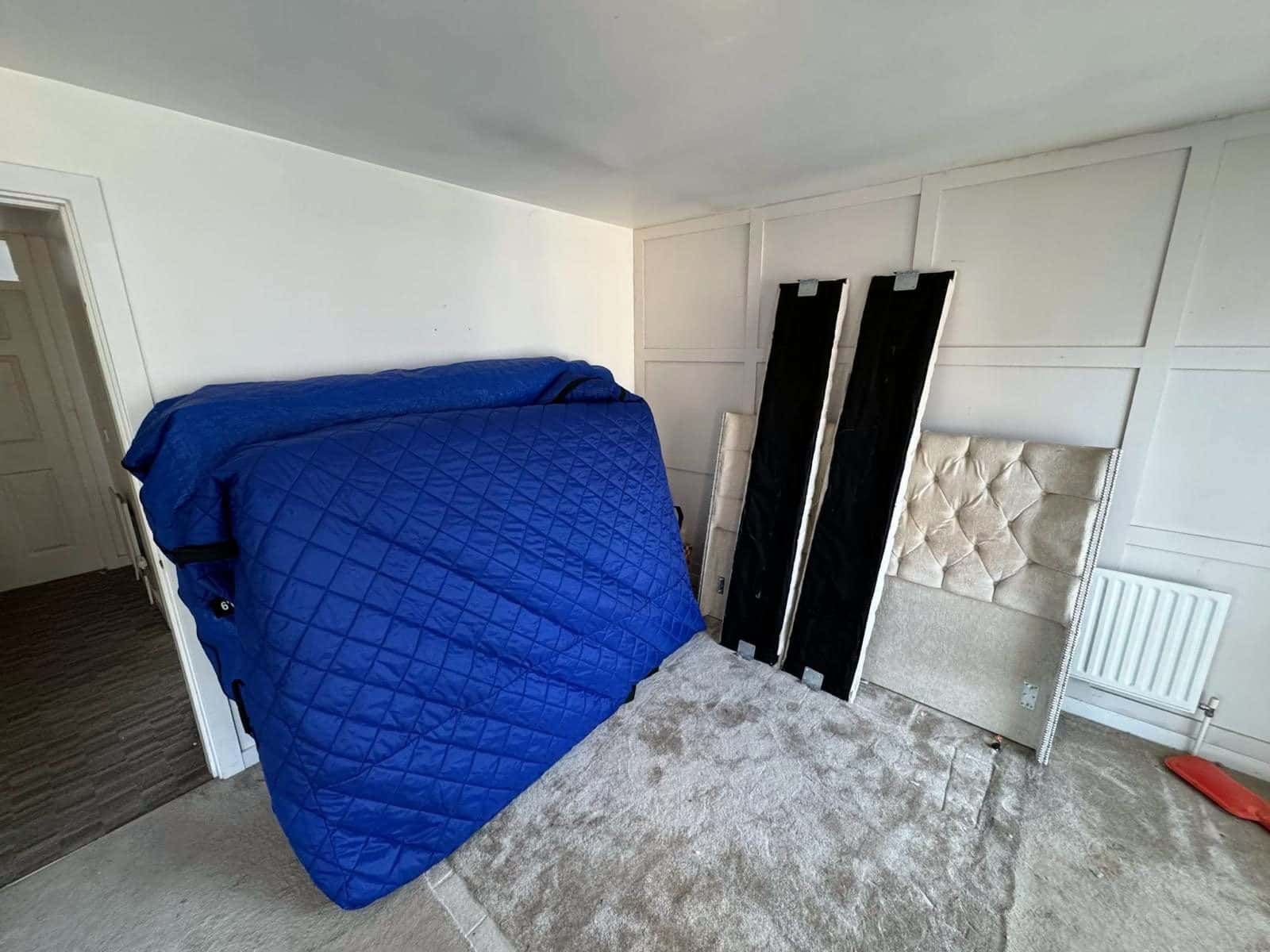 Mattress in a blue quilted cover with the dismantled bed frame beside it