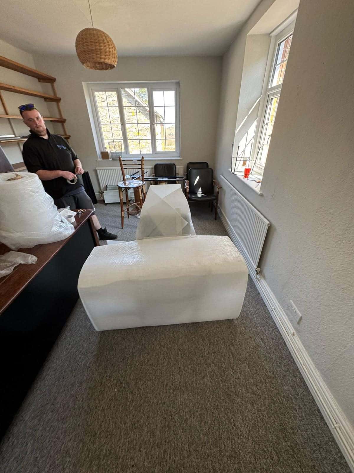 Duffield crew member with bubble-wrapped office furniture in a bright office