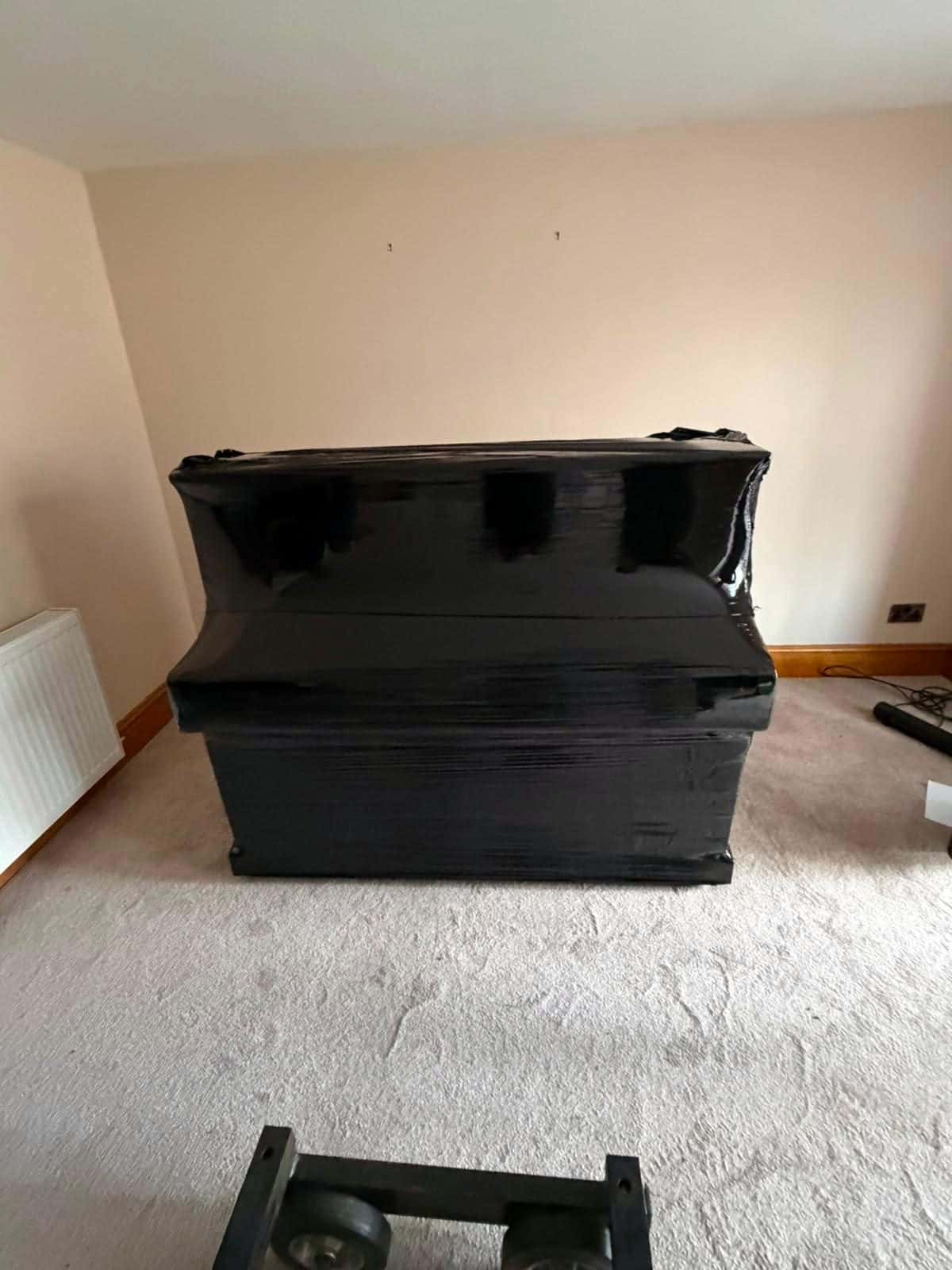 Upright piano wrapped in black stretch film in an empty room, dolly in front