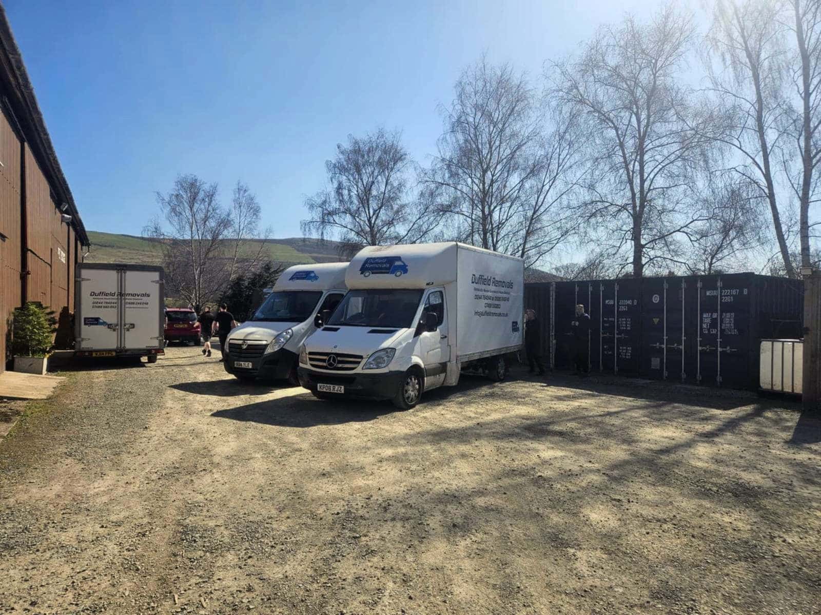 Three Duffield vans in the Rhayader storage yard beside containers