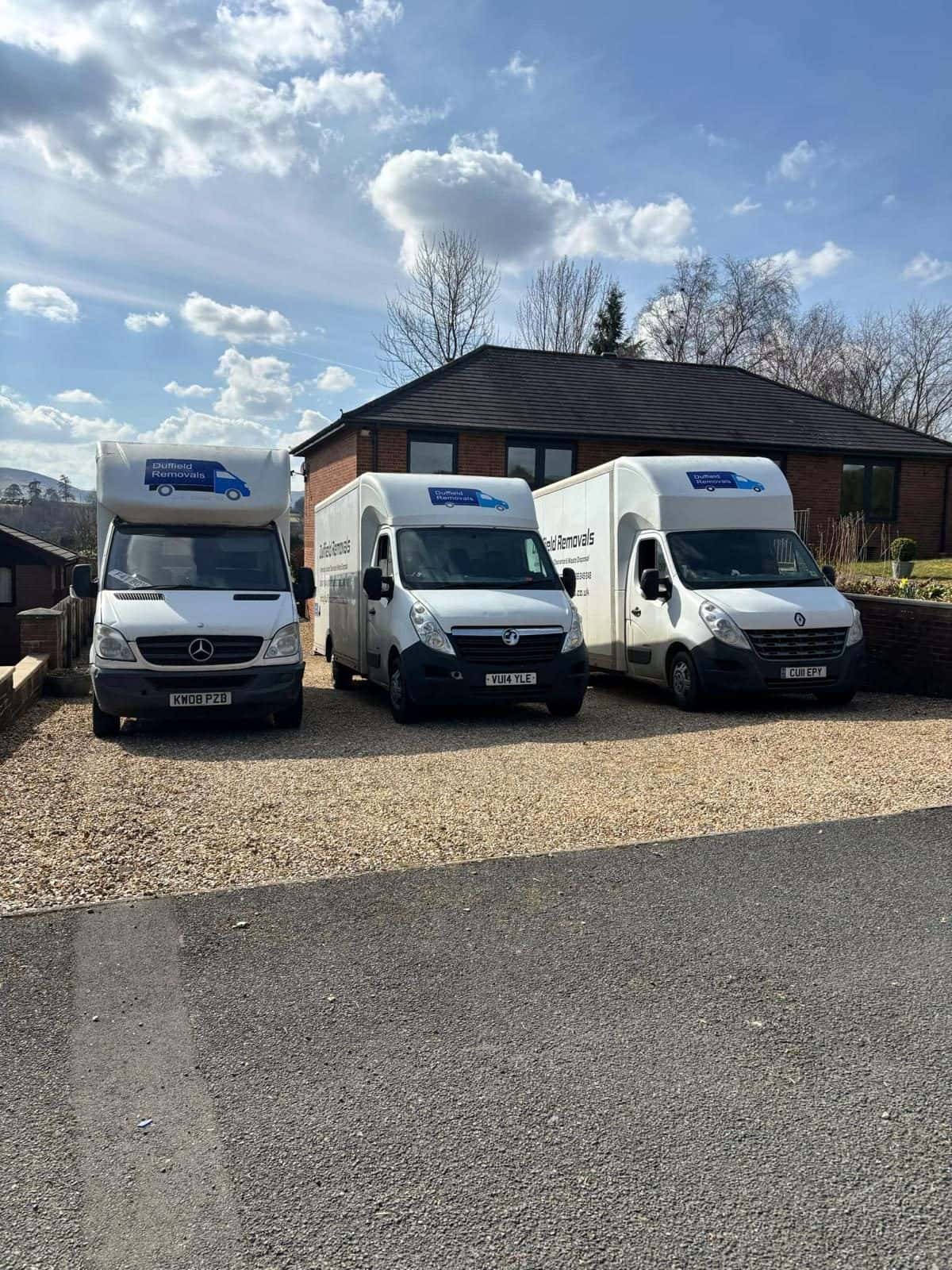 Three Duffield Removals vans parked in a row on gravel with hills behind