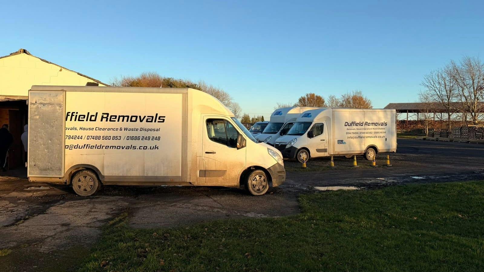 Duffield Removals Luton vans lined up in a yard in low evening sun