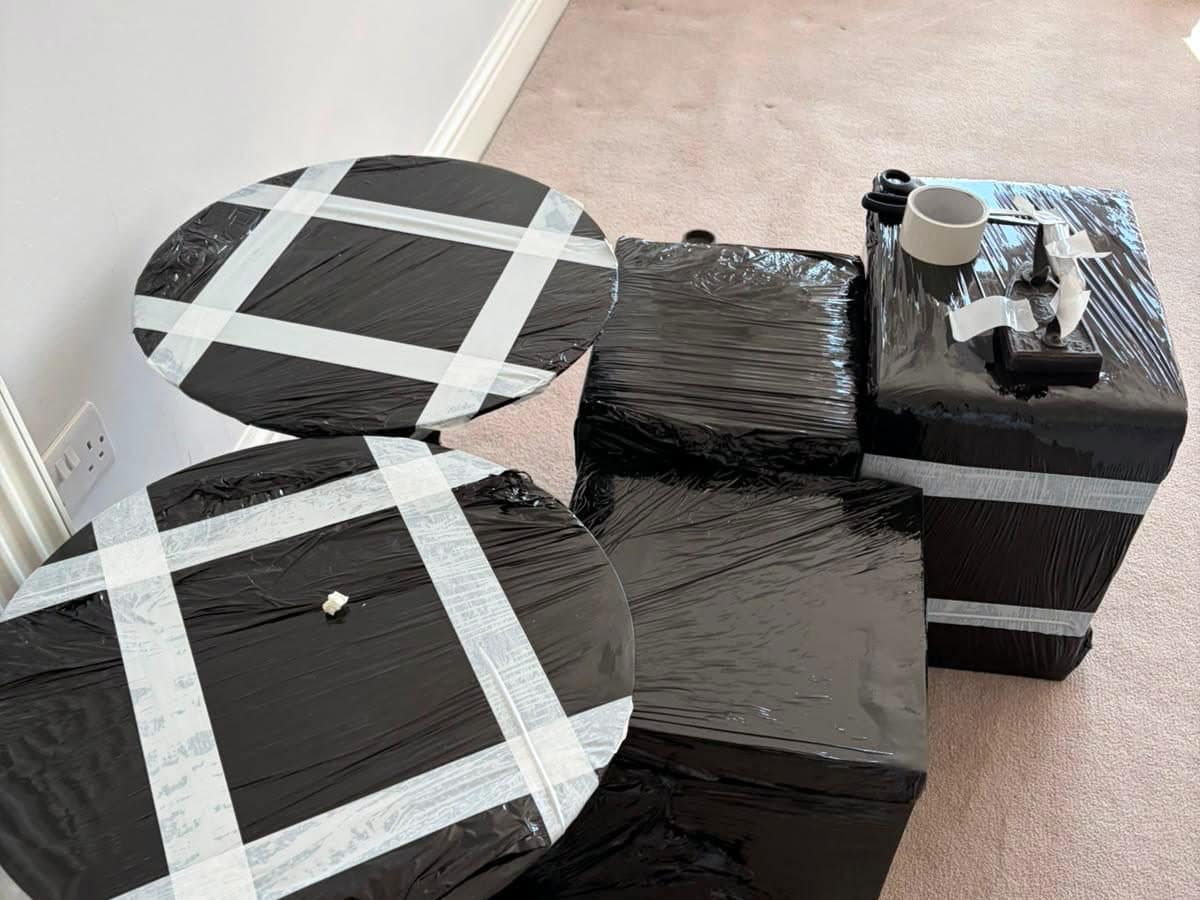 Side tables and cubes export-wrapped in black stretch film with tape crosses on the tops