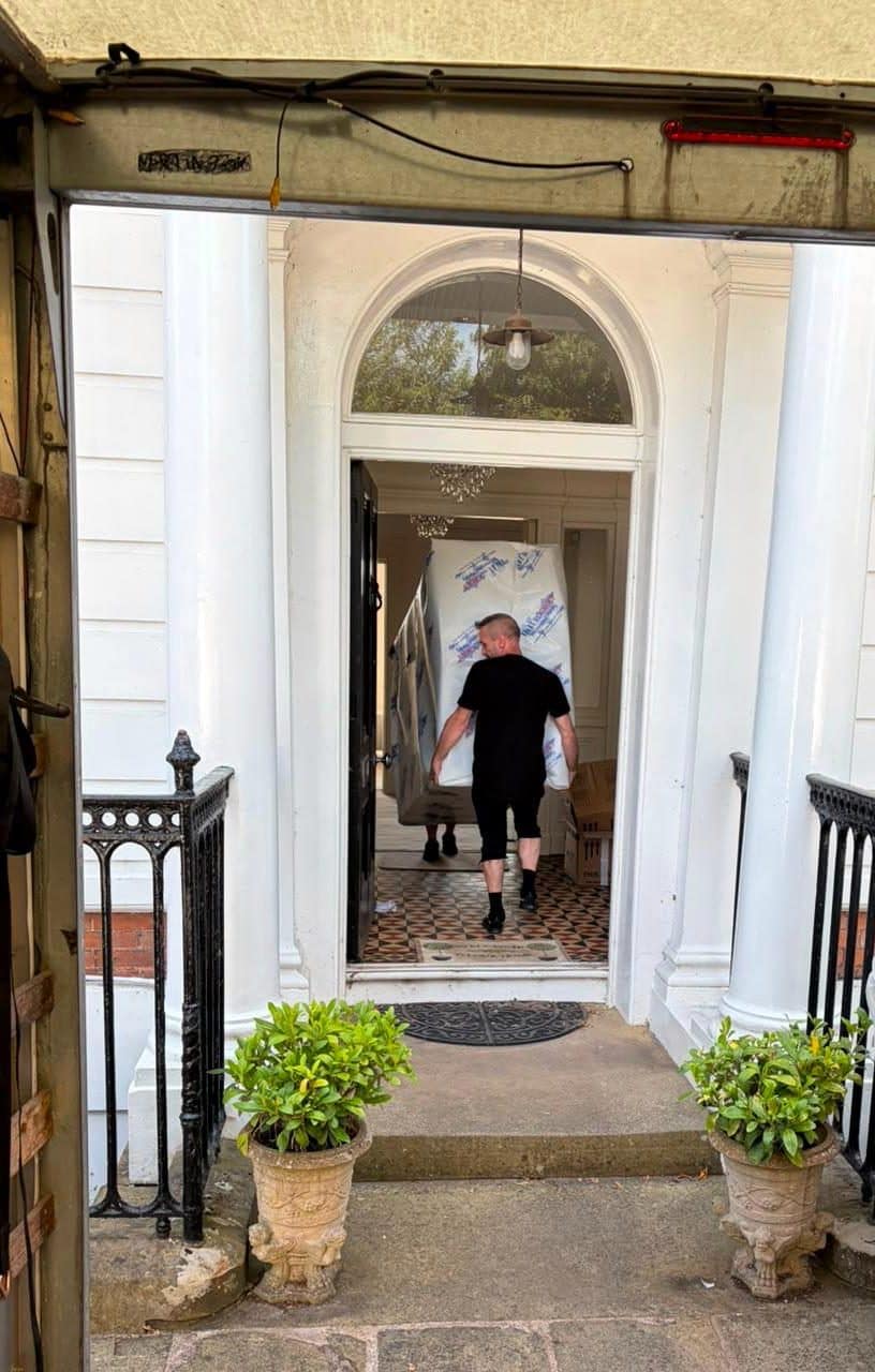 Two Duffield crew carrying a wrapped item through a columned porch