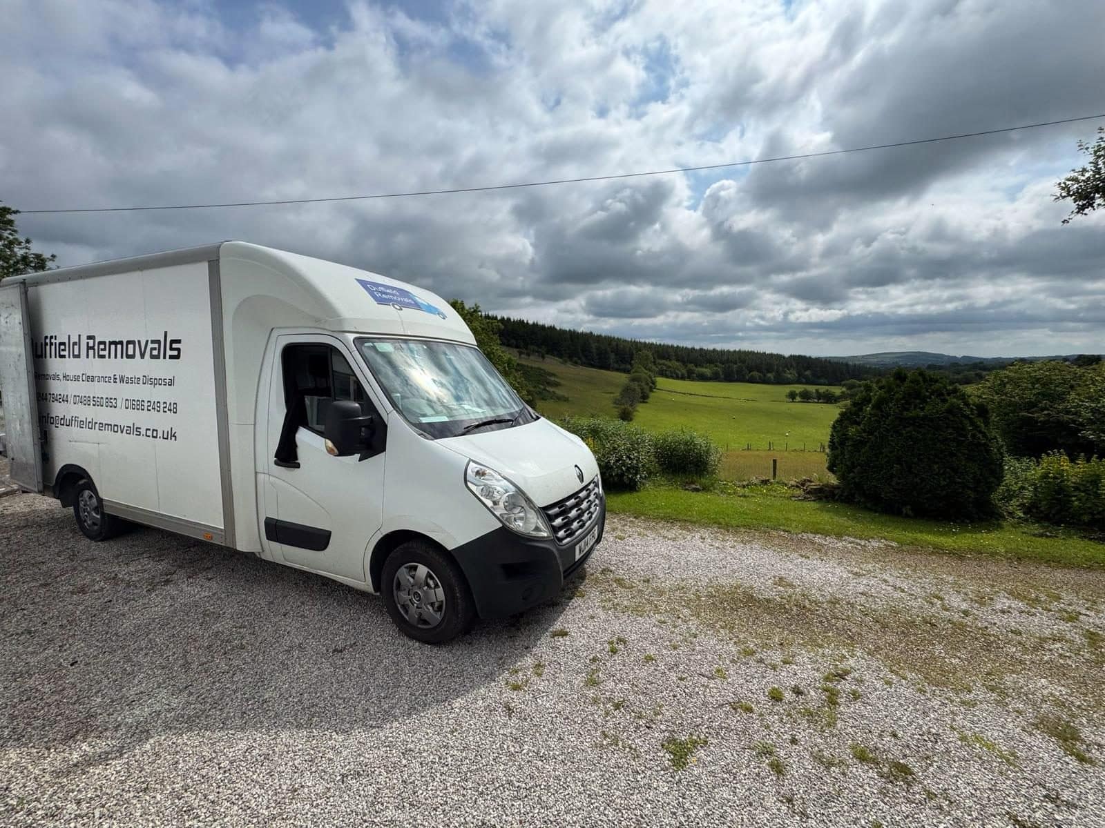 Duffield Luton van on a gravel drive under a dramatic sky, green valley behind