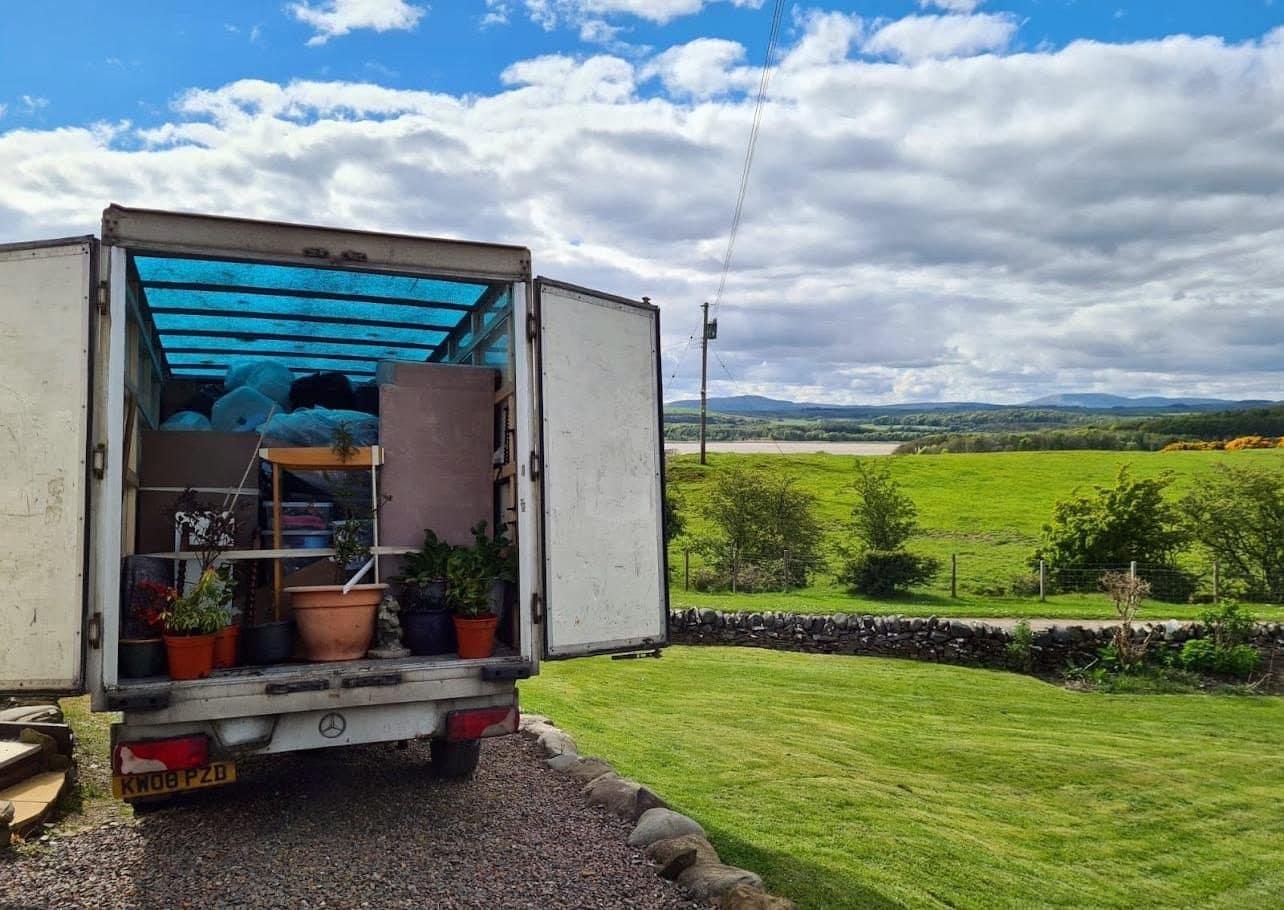 Open Duffield van loaded with plants and furniture, lawn and hills behind