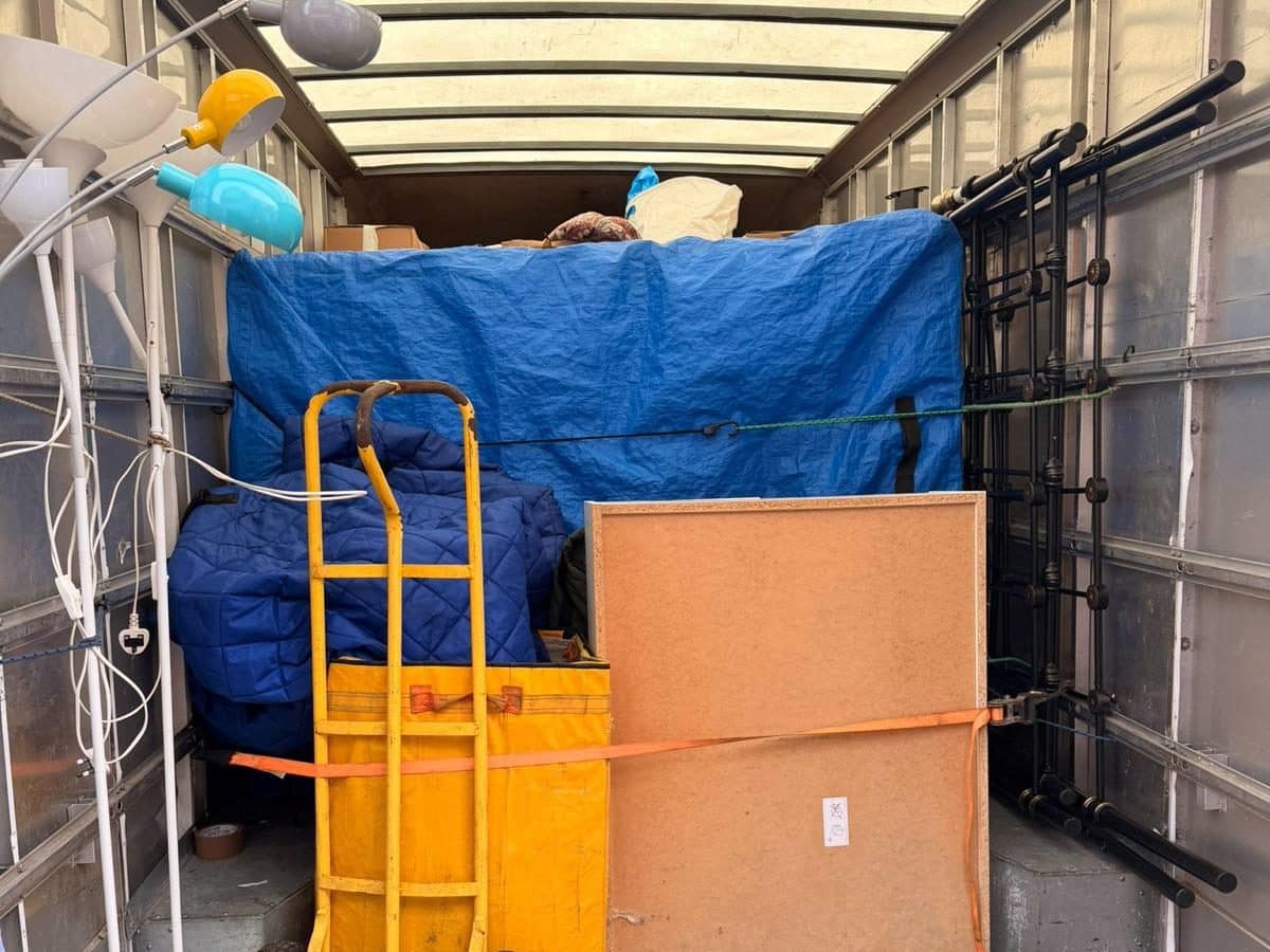 Removal van load secured with an orange ratchet strap, blankets and a sack truck