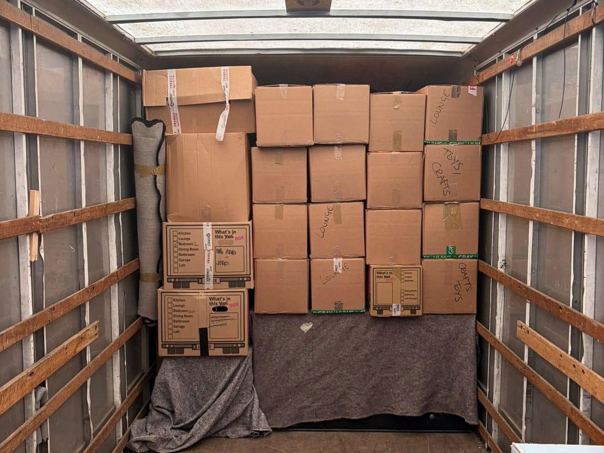 Wall of packed boxes labelled by room stacked on moving blankets inside a removal van