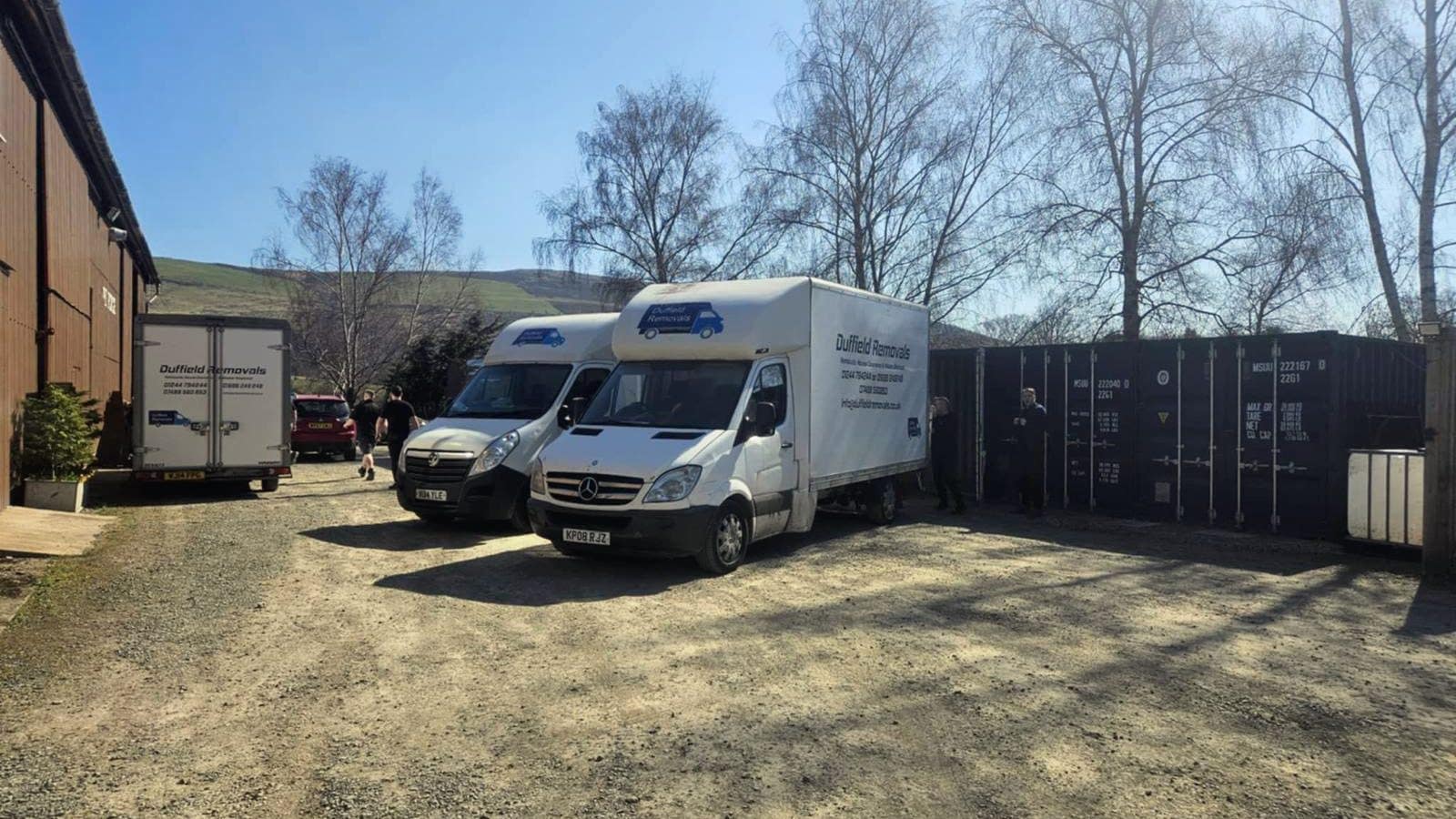 Three Duffield vans in the Rhayader storage yard beside a row of shipping containers
