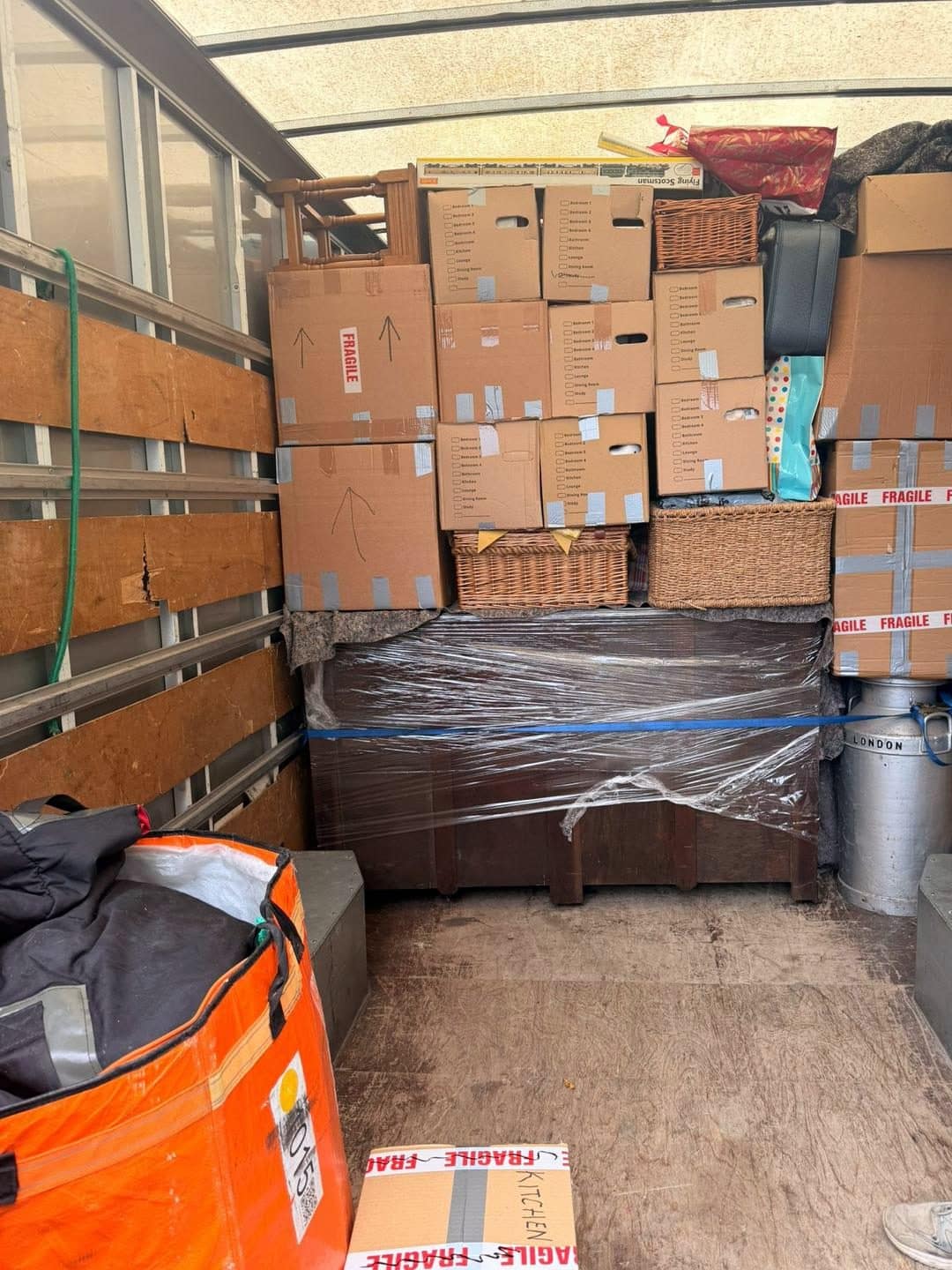 Room-labelled cartons with fragile tape and a stretch-wrapped chest strapped inside a removal van