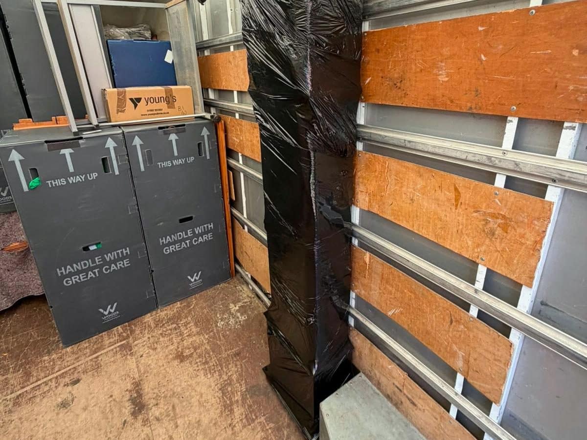 Tall item wrapped head to toe in black stretch film beside wardrobe cartons in a van