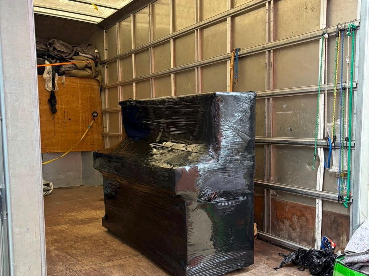Upright piano fully stretch-wrapped and standing inside a Duffield removal van